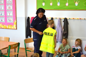 policjantka na spotkaniu z dziećmi ubiera dziecko w żółtą kamizelkę odblaskową