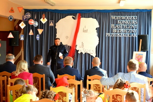 policjant przemawia w tle napis wojewódzki konkurs plastyczny bezpieczny przedszkolak