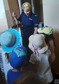 Dzieci w pomieszczeniach dla zatrzymanych oraz policjantka pokazująca kajdanki zespolone