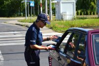 policjantka rozmawiająca z kierowcą samochodu, wręczająca ulotki informacyjne