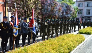stojący policjanci w poczcie sztandarowym, podczas salwy honorowej wykonywanej przez żołnierzy