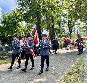 trzech policjantów idących w poczcie sztandarowym, policjant w środku trzyma sztandar