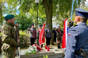 trzech policjantów umundurowanych stojących ze sztandarem przy pomniku żołnierza Poskiego