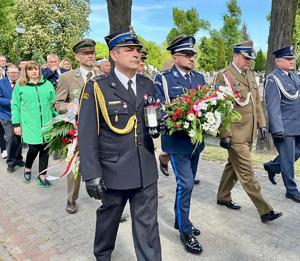 komendant idący w obecności przedstawicieli innych służb mundurowych niosący patriotyczną wiązankę