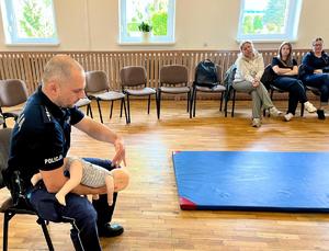 policjant pokazuje na fantomie niemowlaka jak spowodować odksztuszenie dziecka