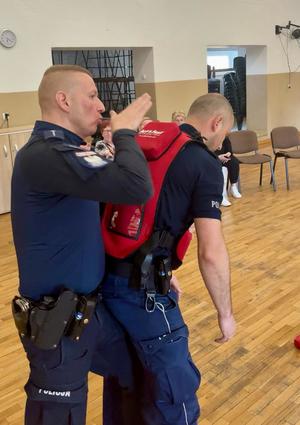 policjant pokazujący na drugim policjancie jak prawidłowo uderzać w plecy przy zakrztuszonej osobie