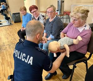 policjant pokazujący, kobiecie jak prawidłowo ułożyć dziecko na ręce przed uderzeniami w plecy w przypadku zadławienia się dziecka.