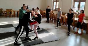 uczestniczki kursu ćwiczące kopnięcia z kolana w ochraniacz trzymany przez policjanta