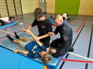 policjant pokazujący dwóm chłopcom chwyt leżąc na materacu