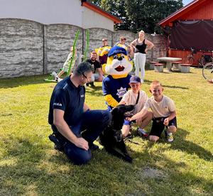 policjant ze swoim psem służbowym na zewnątrz, dzieci głaszczą leżącego na trawie psa