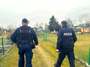 dwóch policjantów idących ścieżką przez ogródki działkowe
