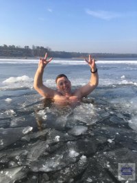 mężczyzna stojący w wodzie z uniesionymi rękami, wokół mężczyzny na powierzchni wody pływające kawałki lodu