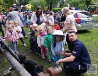 policjant kucający przy dziecku ubranym w policyjny sprzęt, kamizelka, kask tarcza