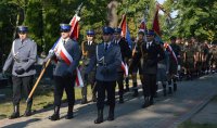 policyjny poczet sztandarowy składający się z trzech policjantów, maszerujących w stronę pomnika żołnierza polskiego