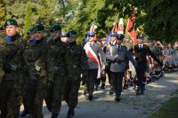 policyjny poczet sztandarowy składający się z trzech policjantów, maszerujących w stronę pomnika żołnierza polskiego