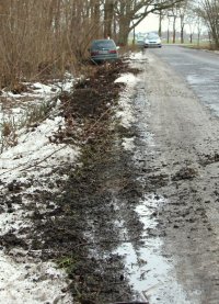 ślady opon na grząskim podłożu prowadzące do stojącego w rowie tyłem samochodu osobowego.