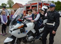 dziecko siedzące na policyjnym motocyklu obok stojący umundurowany policjant